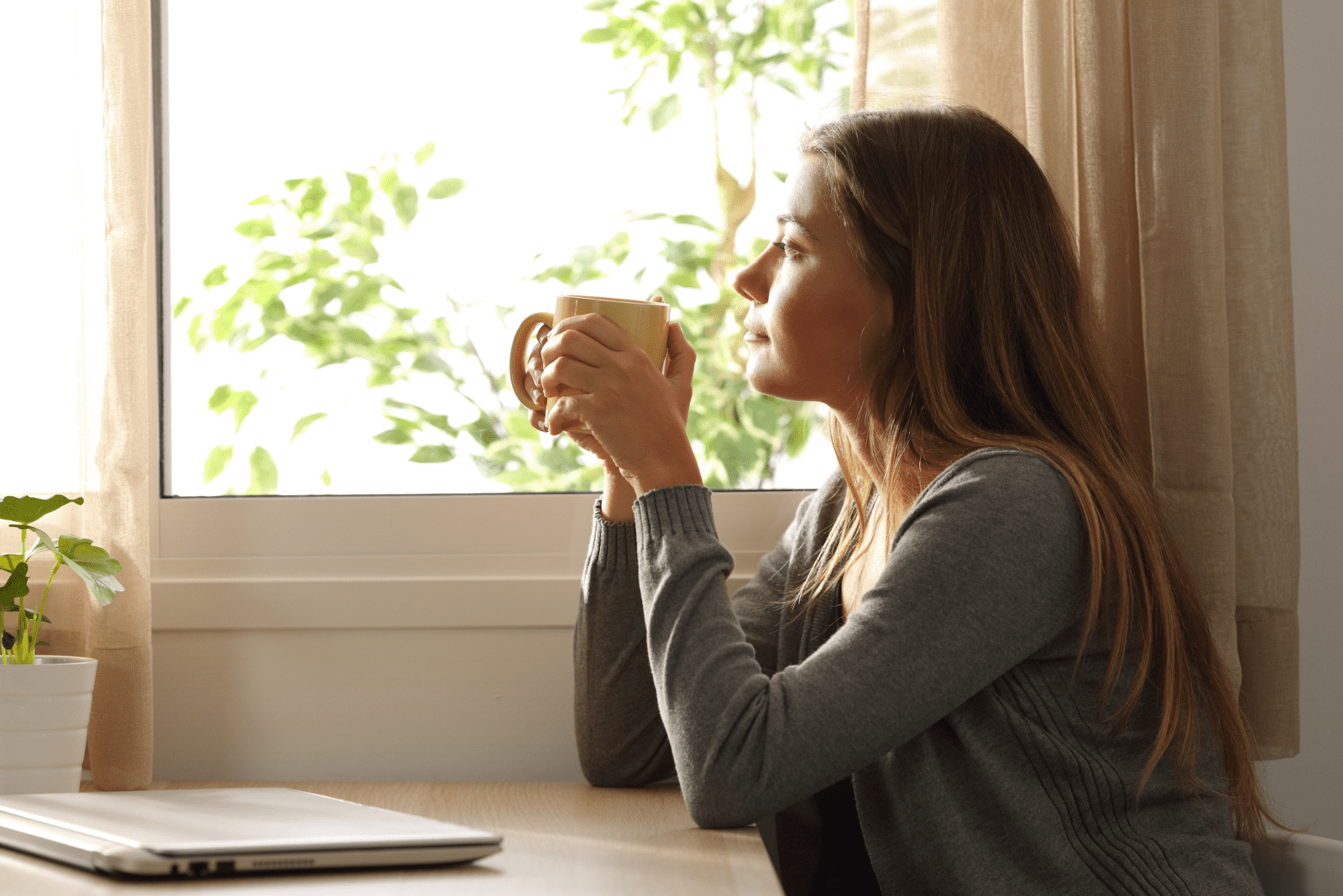 pensive woman sitting at the table and holding a cup in her hand