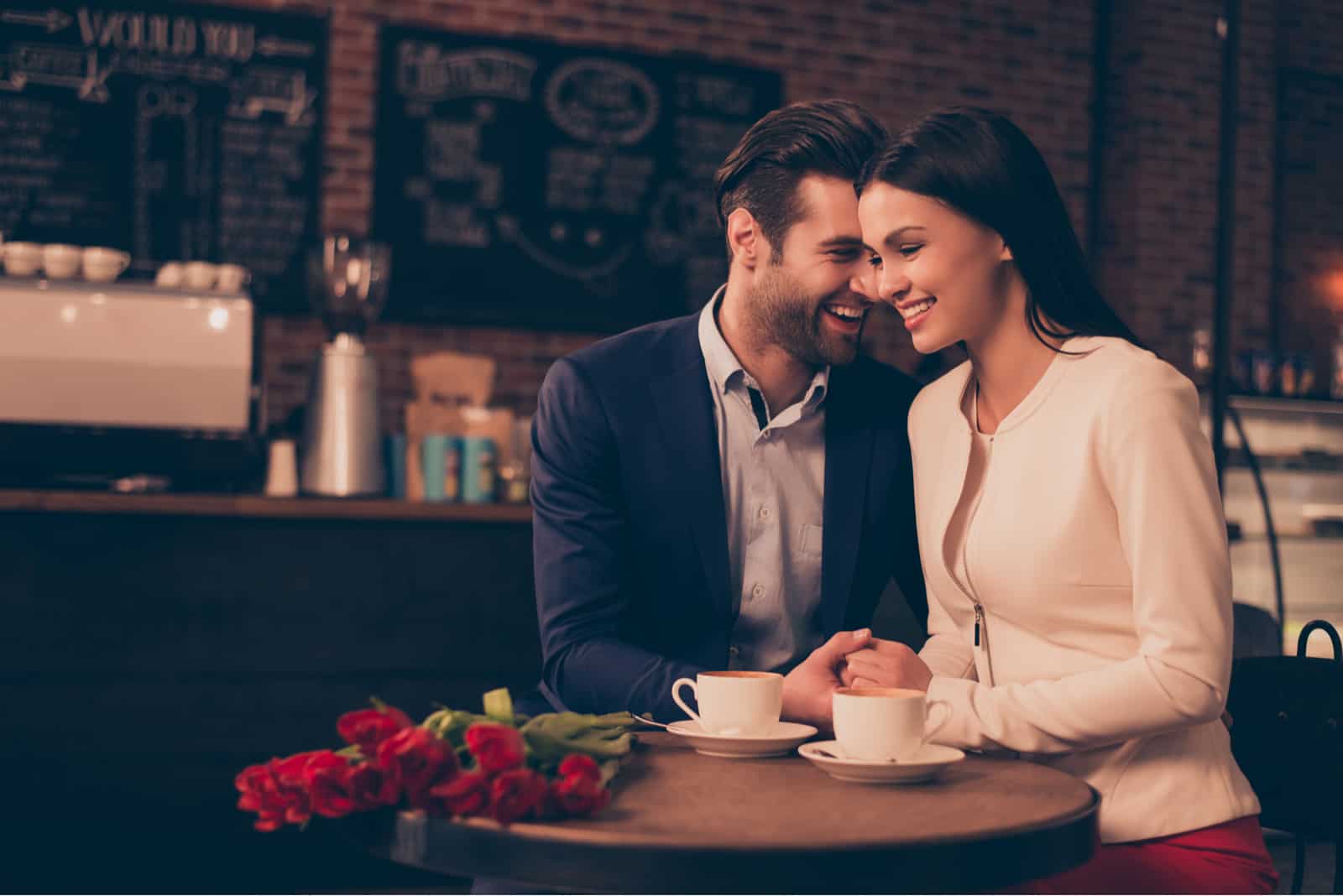 a smiling man and woman holding hands as they sit at the table