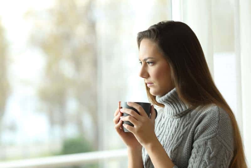 A thoughtful woman holds a cup of tea, looking into the distance