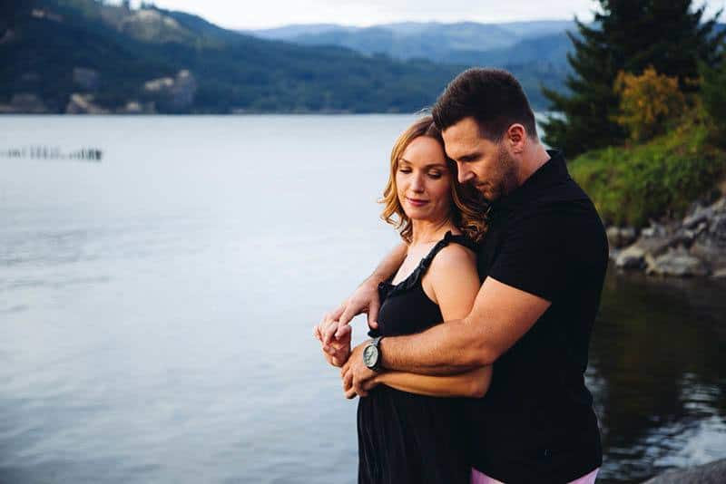 A man hugs a woman by the lake, capturing a beautiful moment of support and love.