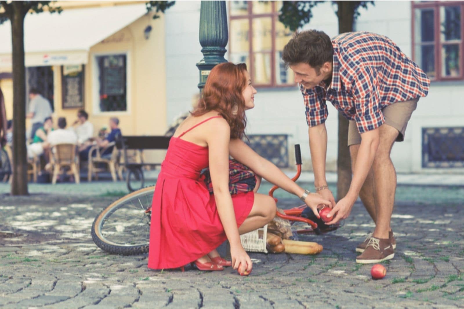 young man helping a woman pick up the fruits fell from the bike on the road