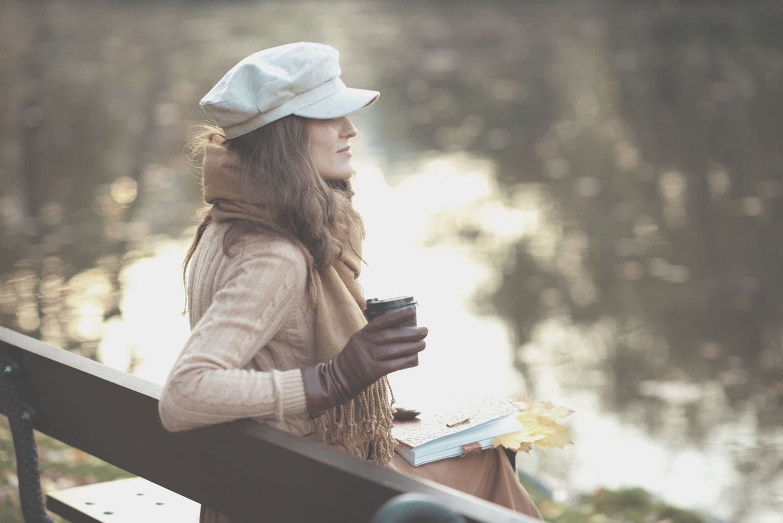 pensive woman with notebook and a cup of coffee and yellow leaves in the park