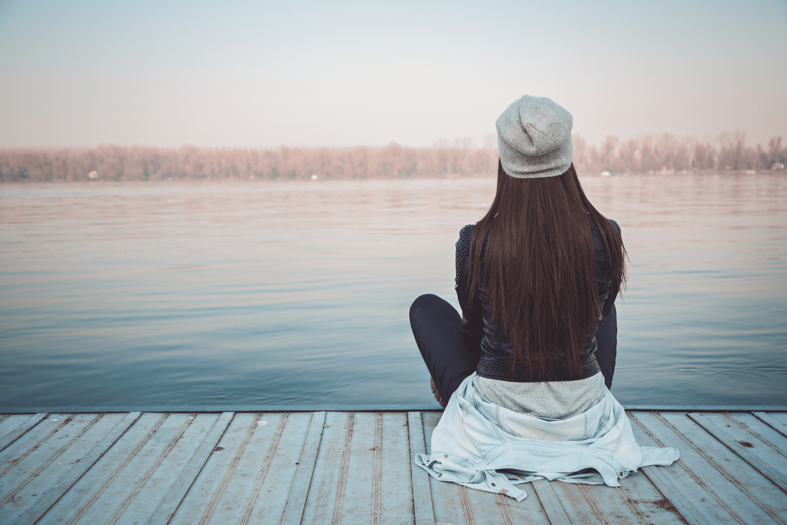 a woman with a cap on her head is sitting on the pier
