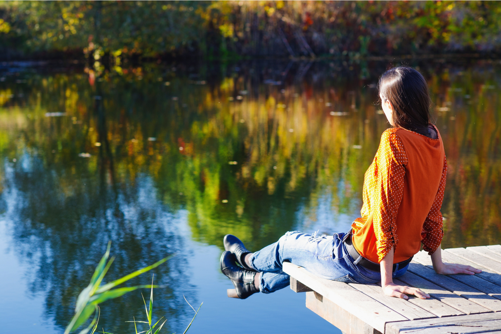 photo of a woman sitting on a dock and looking at a lake