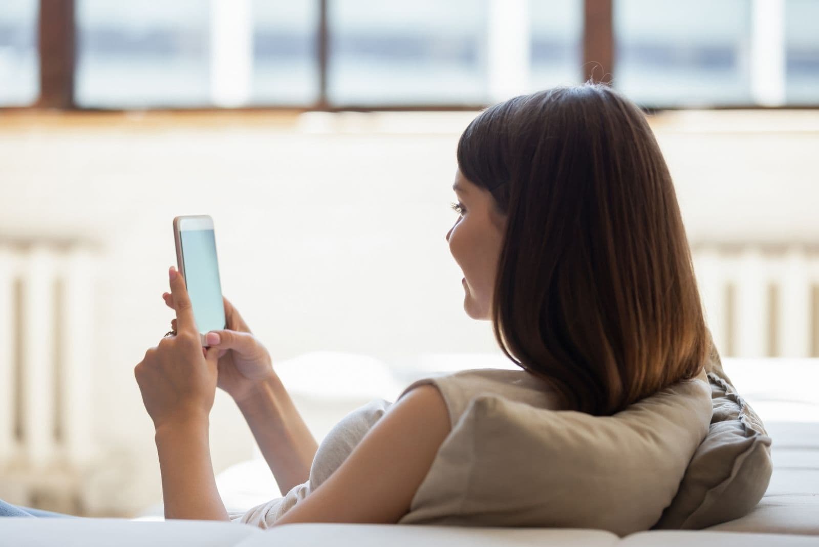rear view of a woman browsing thru her smartphone chilling in the couch of the living room