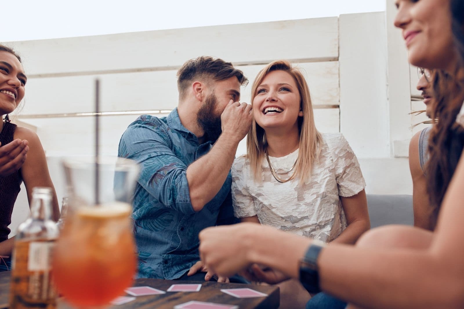 young people sitting together in a party man whispering on the woman laughing