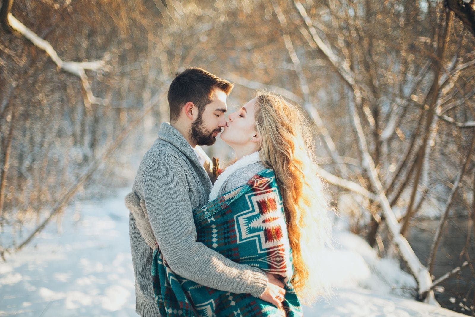 romantic man and woman kissing covered with thick clothed around hugging in the middle of winter forest