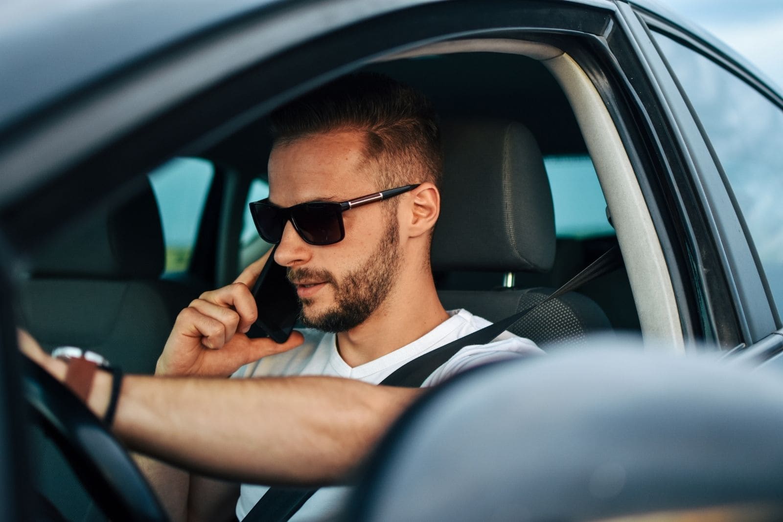 man driving a car answering the phone wearing sunglasses