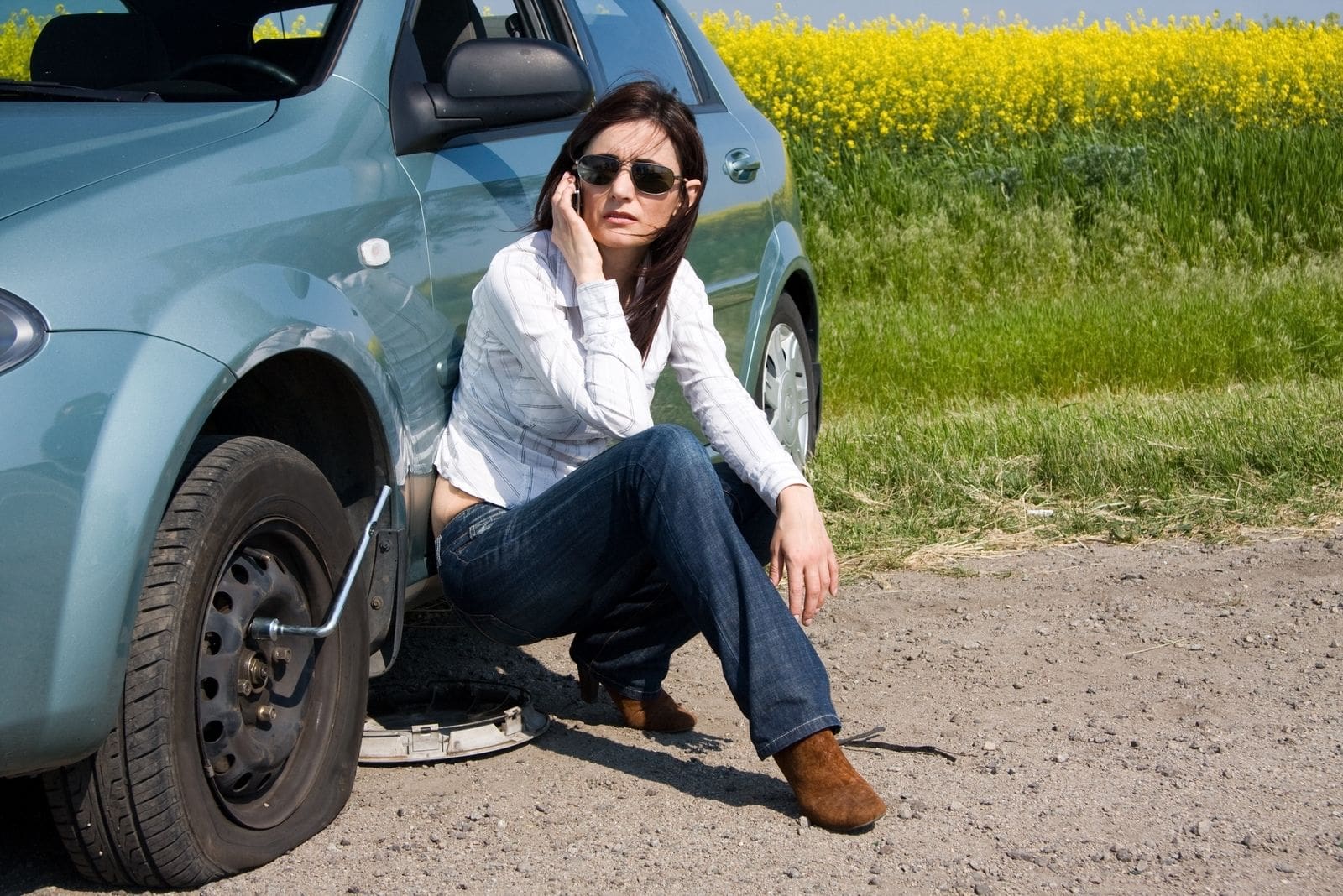 woman in distress calling sitting beside her car with broken tire