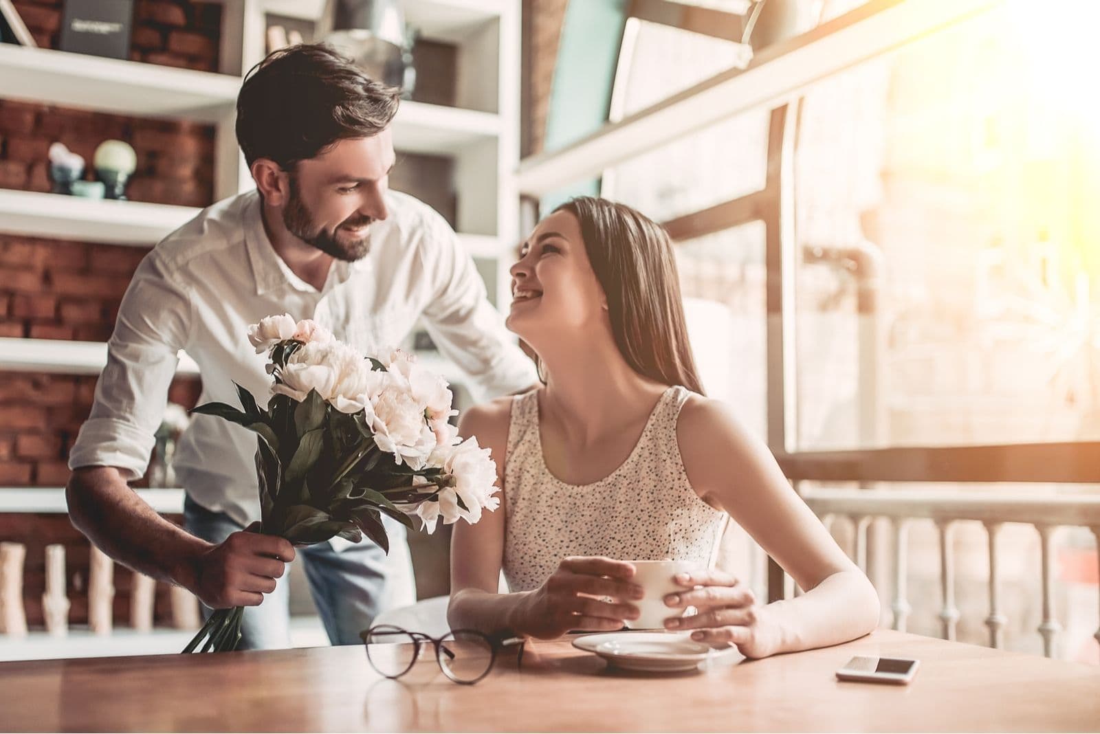 sweet guy surprising her girlfriend with flowers while drinking her coffee in a cafe