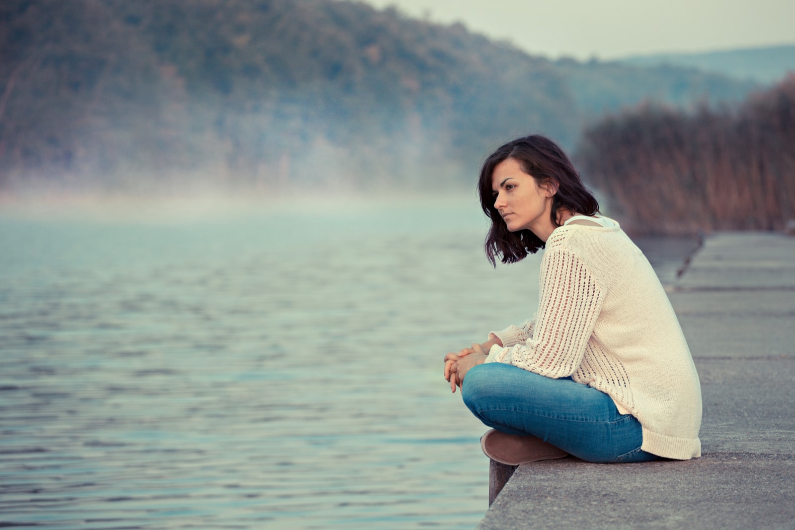 pensive woman sitting by the lake
