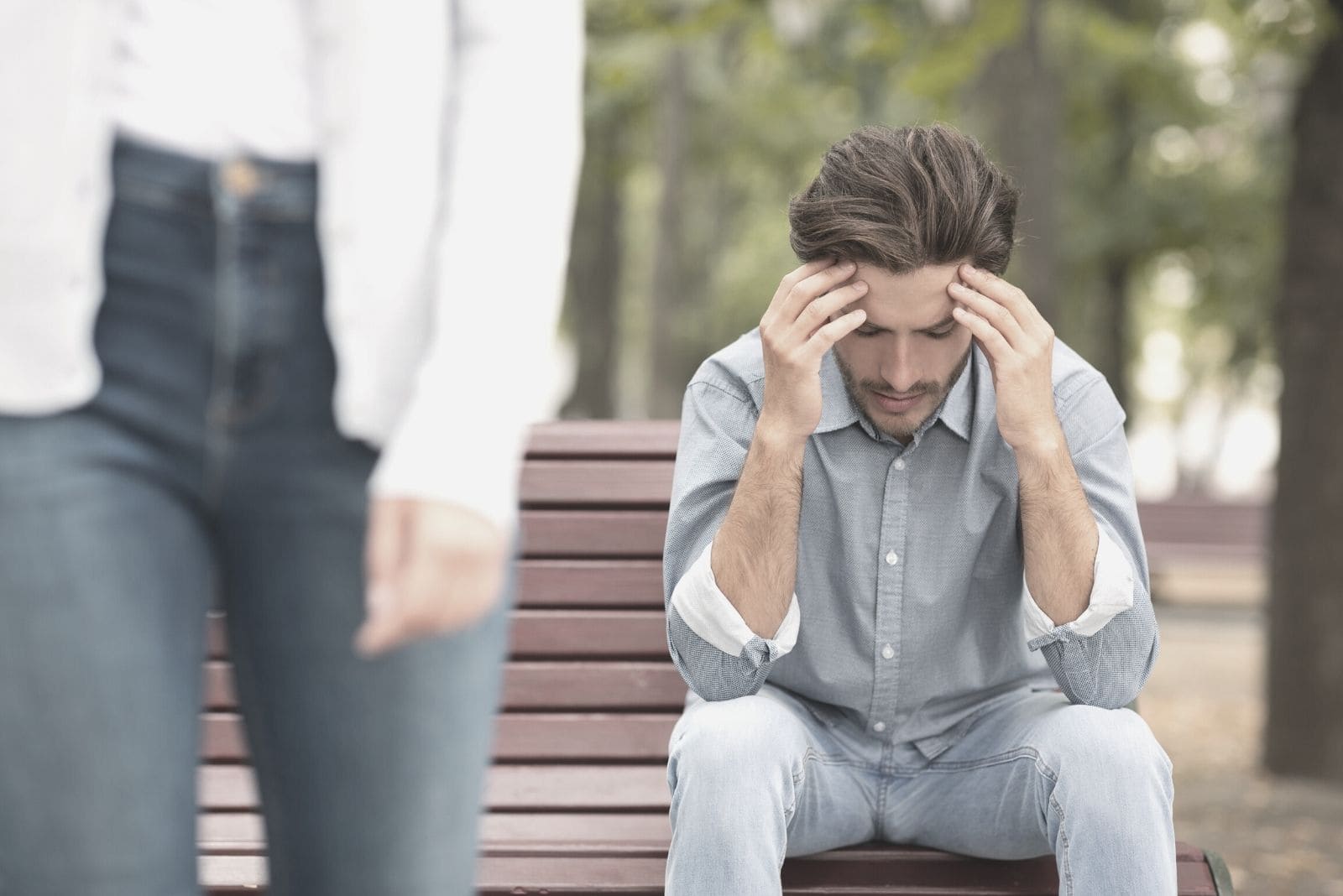 young couple divorce concept man sitting on an outdoor bench while woman walk away